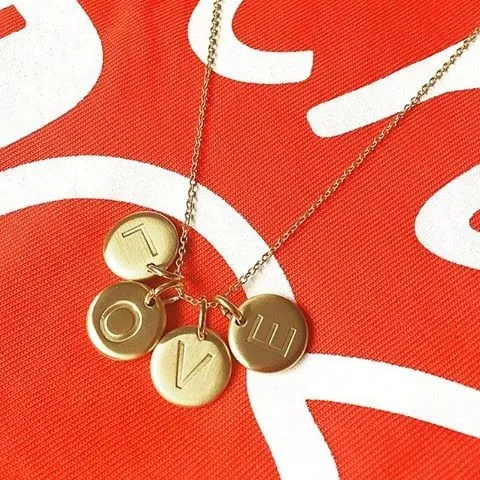 NÆRBILDE AV 4 MATTE GULL BOKSTAVSANHENG FRA CHARMENTITY PÅ RØD BAKGRUNN